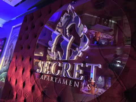 Logo Secret Apartments na pikowanym zagłówku łóżka